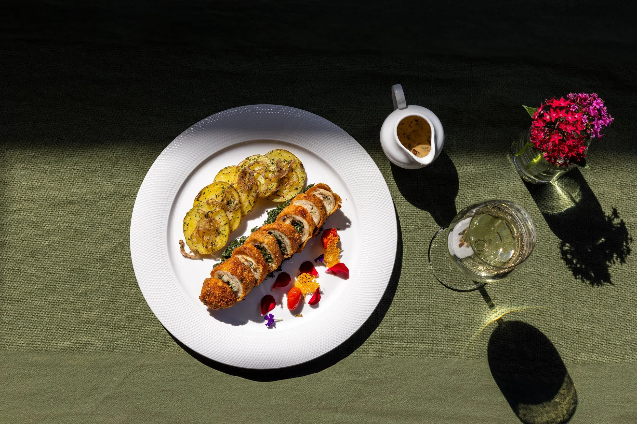 Overhead view of a plated dish with edible flowers and white wine on a green tablecloth