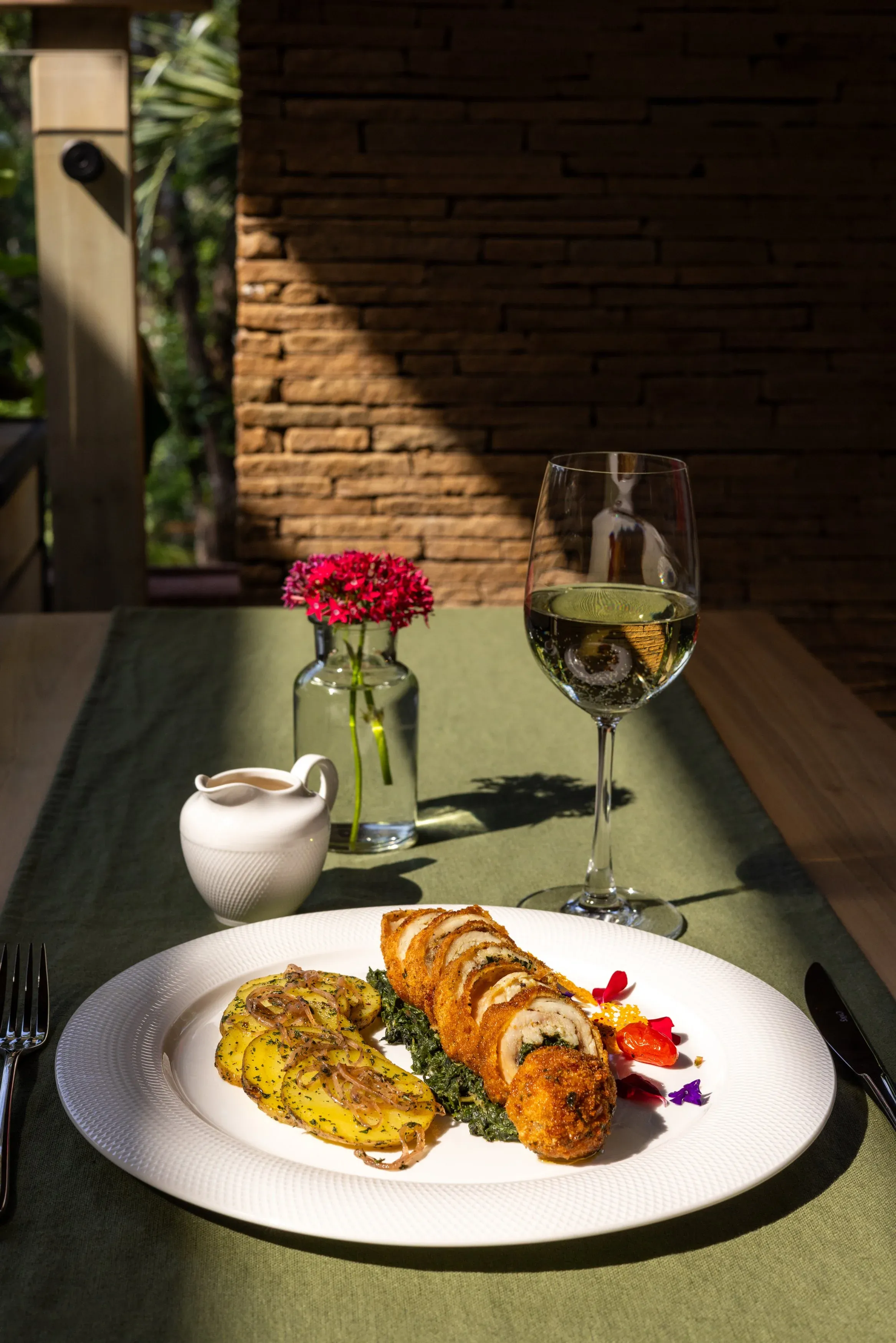 A plated dish on a green tablecloth beside a glass of white wine and fresh flowers