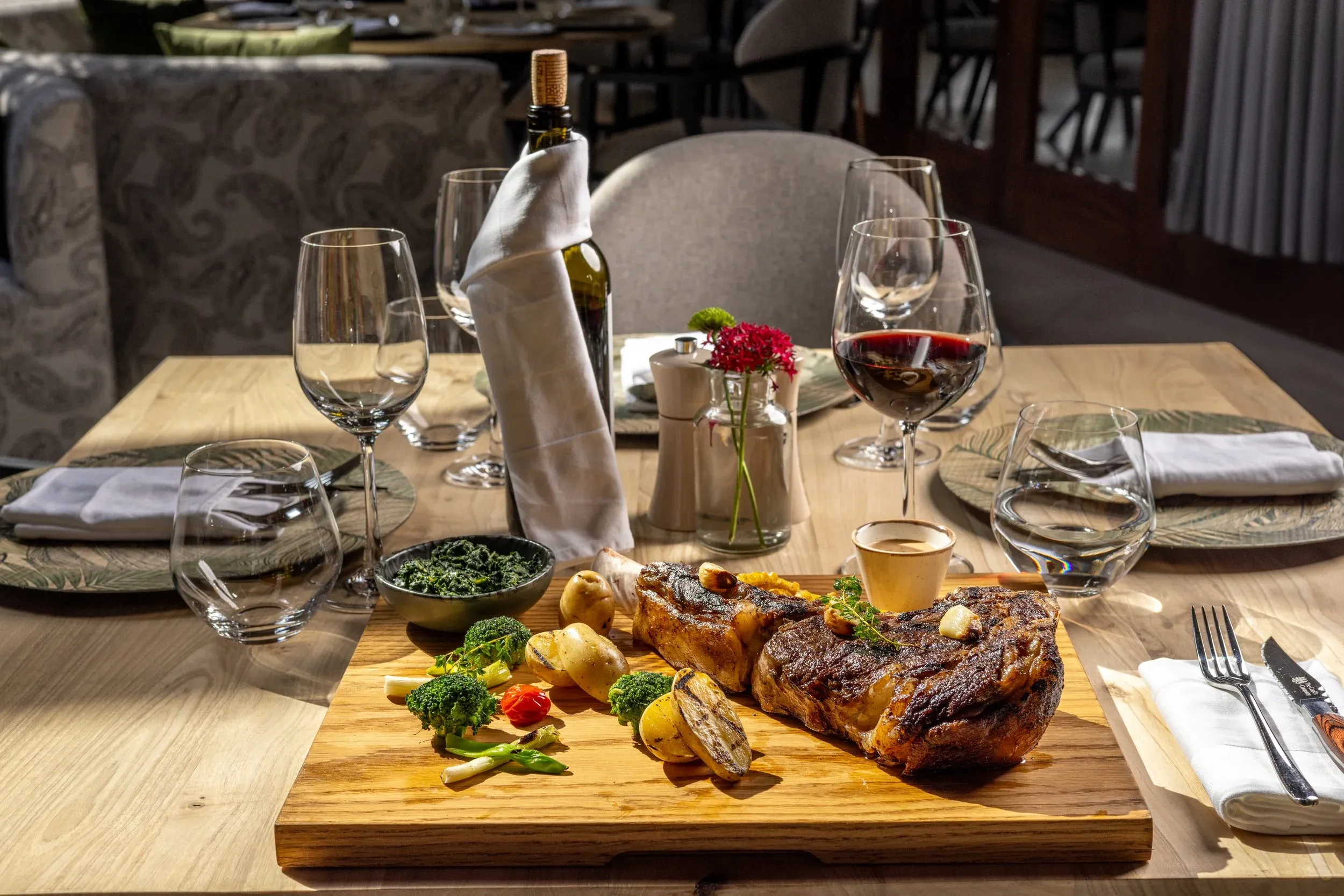 A carved roast on a wooden board with sides and red wine