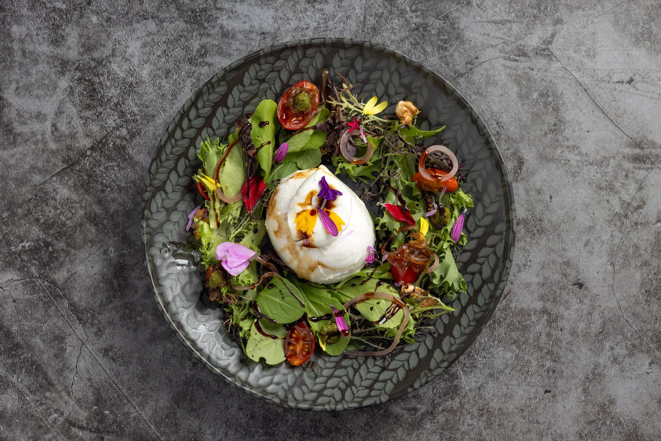 Overhead view of a burrata salad with edible flowers