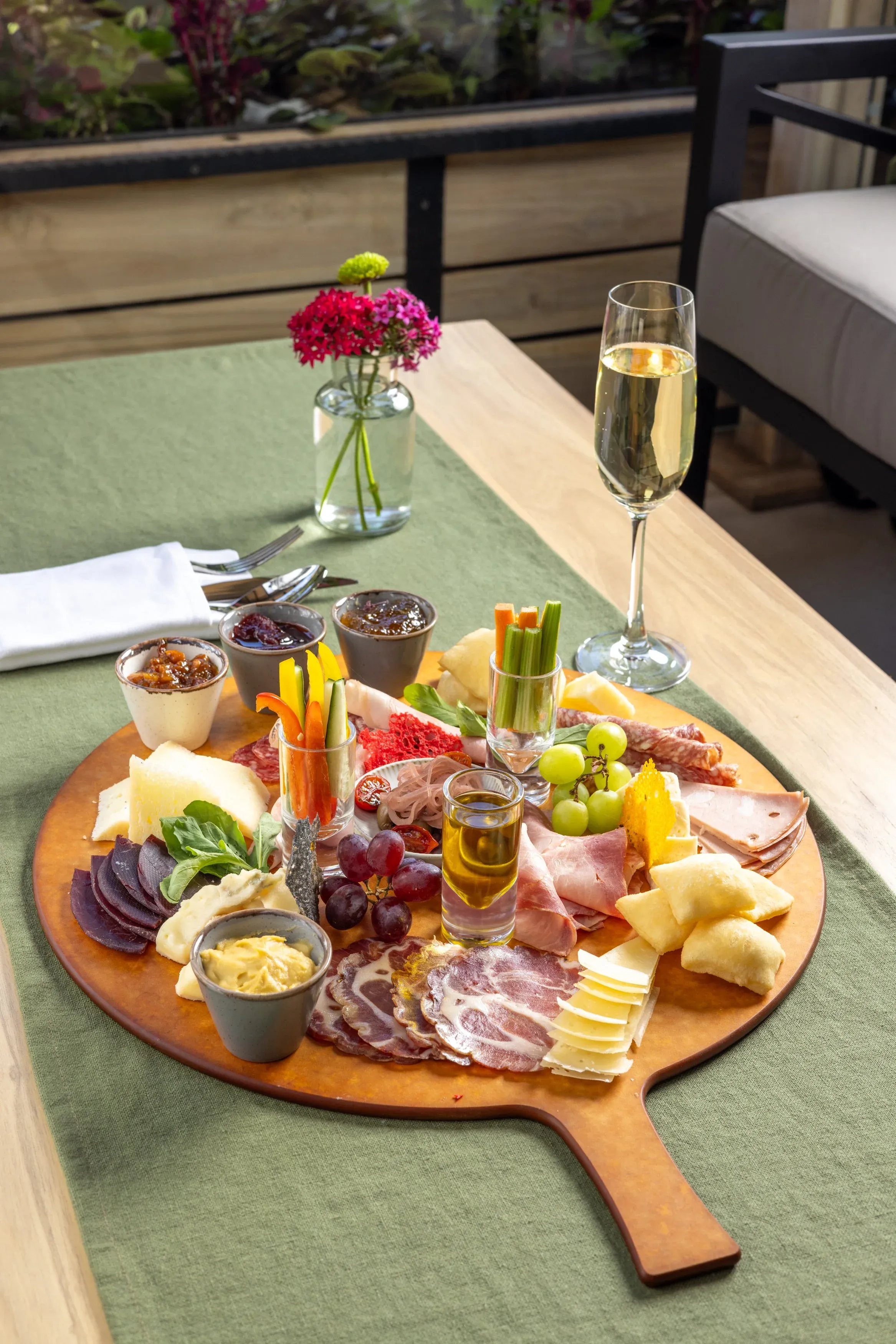 A charcuterie and cheese board on a green table runner with white wine