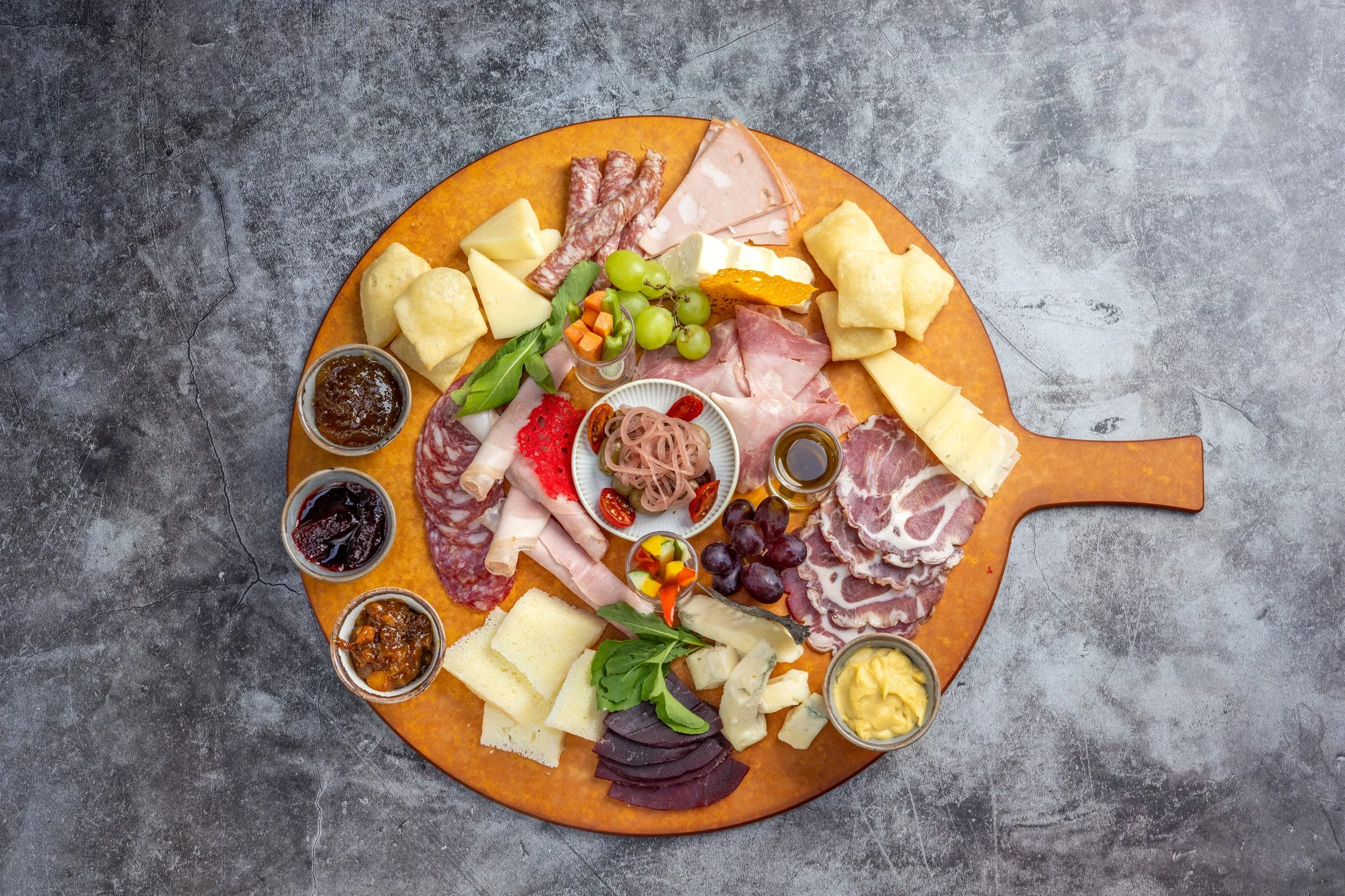 Overhead view of a charcuterie and cheese board with dips and fruit