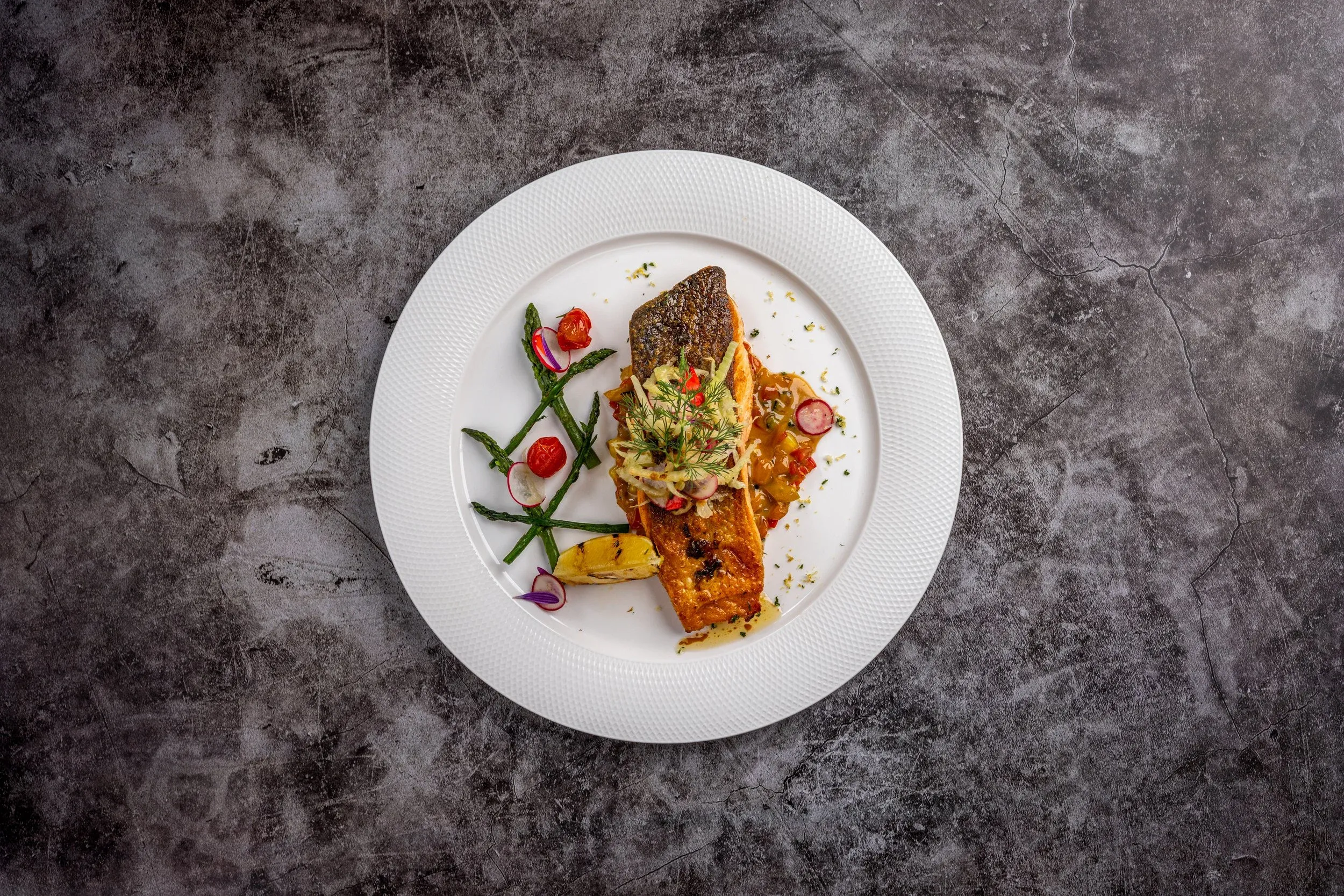 Overhead view of grilled fish with vegetables on a white plate