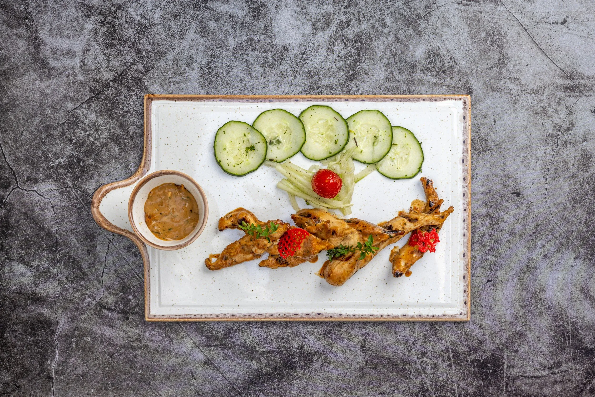 Overhead view of a skewered starter with cucumber slices and dipping sauce